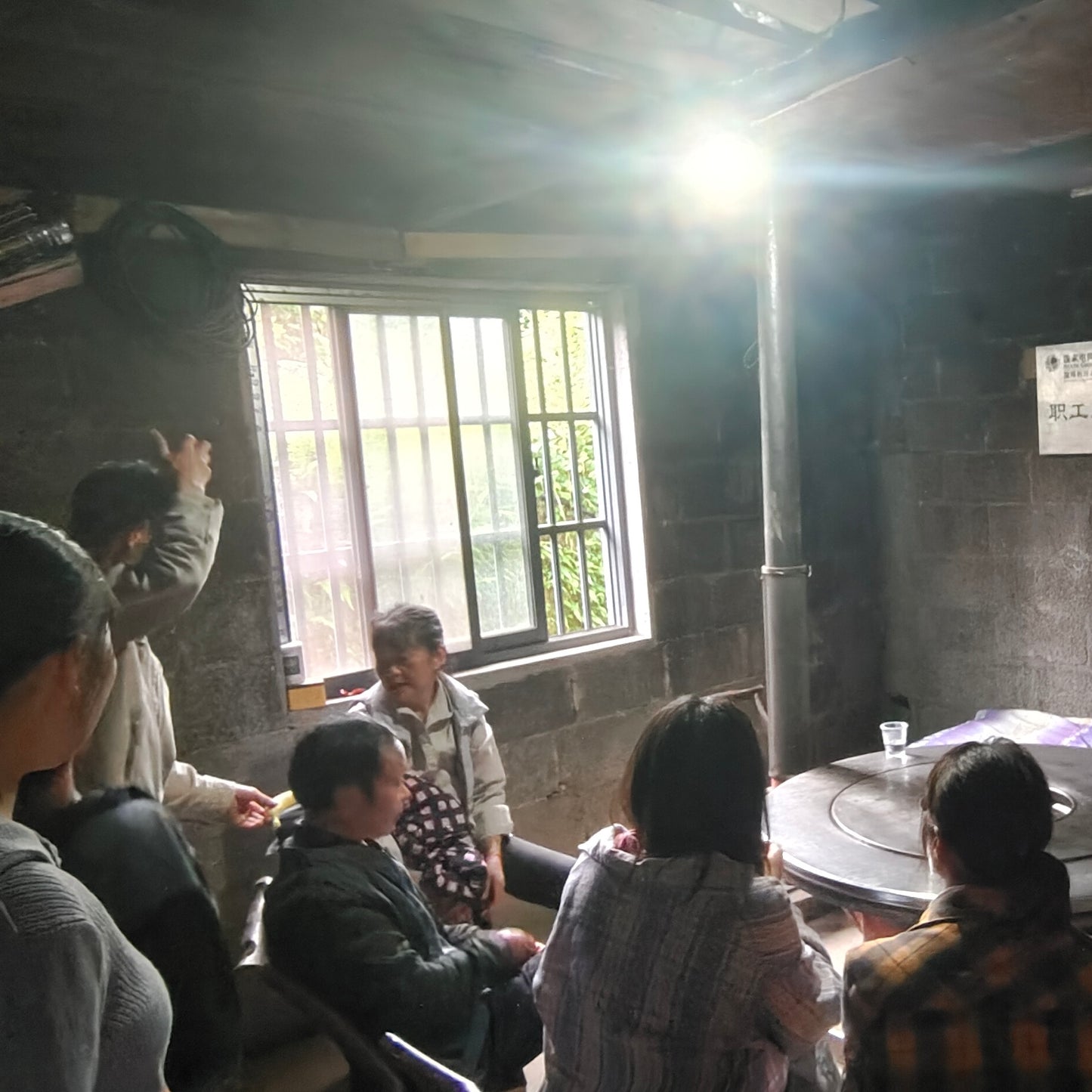 tea farmers sitting around a table in a dimly lit room with a window in the background.