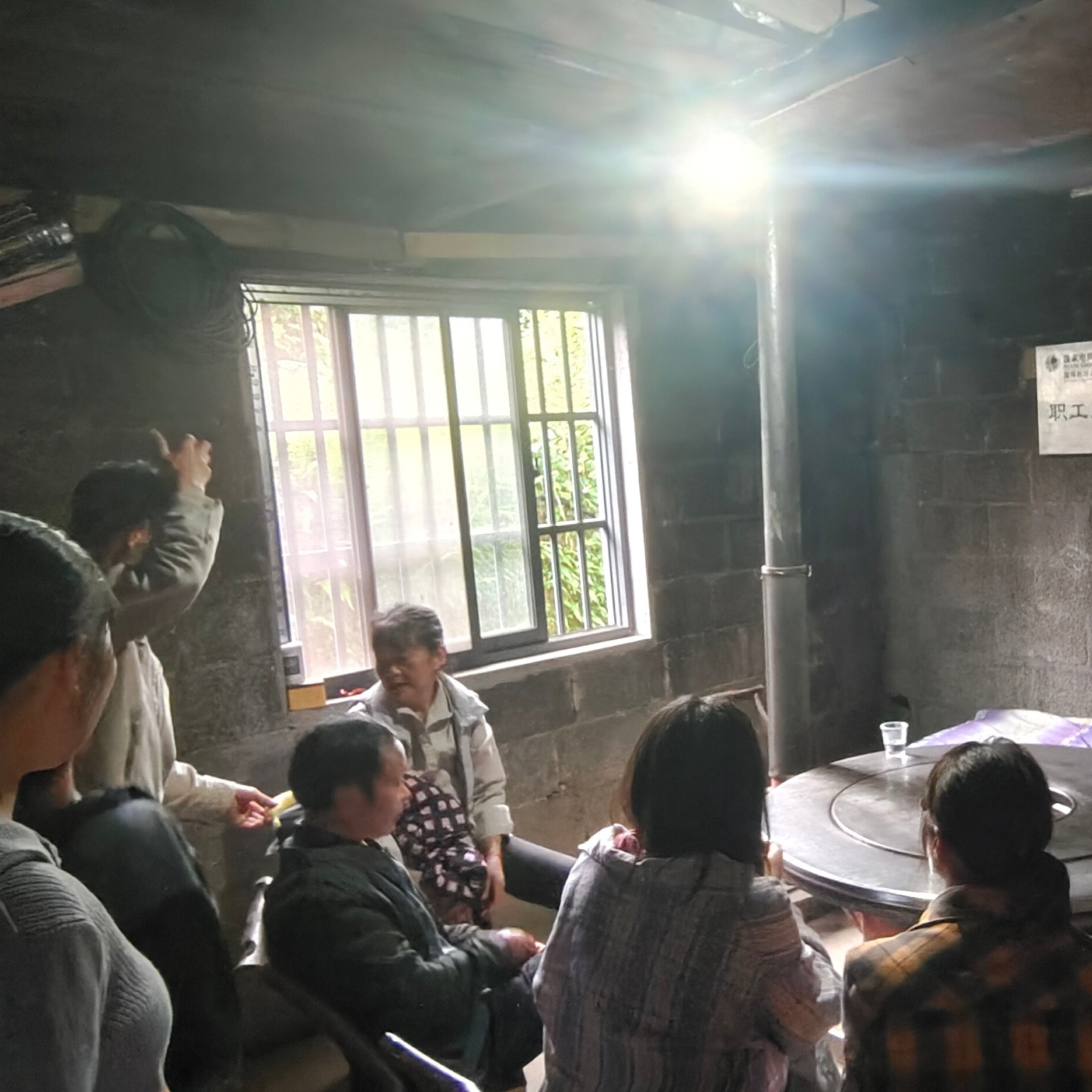tea farmers sitting around a table in a dimly lit room with a window in the background.